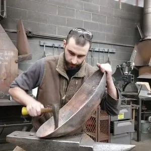 Editor Addison de Lisle hammering on a concave piece of metal atop an anvil.