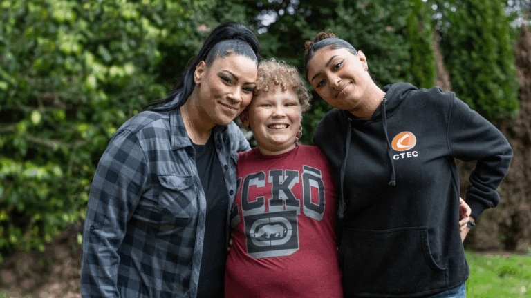 Three people stand smiling in front of trees