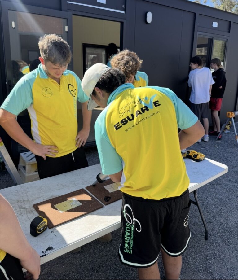 Three young men in yellow and turquoise polo shirts work on a construction project.
